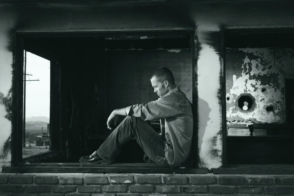 A young man sits pensively in a derelict building, embodying solitude and contemplation.