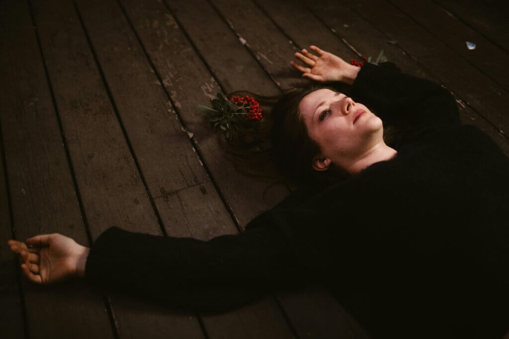 A contemplative woman lies on a wooden floor, evoking introspection.