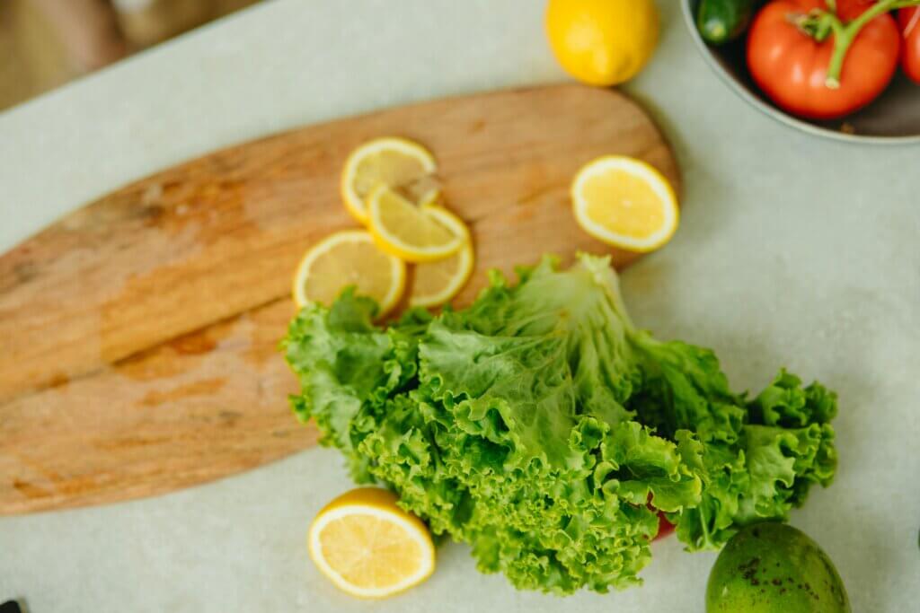 Close-up of organic lettuce, lemon slices, tomatoes, and cucumber on a wooden chopping board. Perfect for healthy eating concepts.